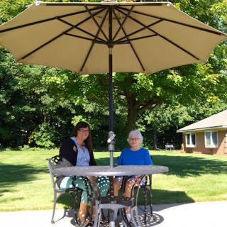 Two individuals enjoying a sunny day under an umbrella, engaged in conversation at a table.