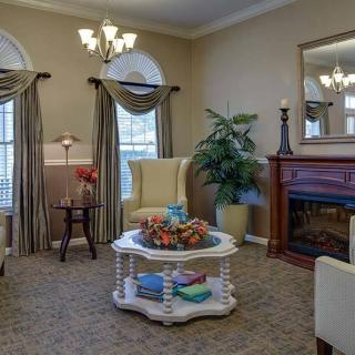 A cozy living room with elegant decor, featuring a fireplace, armchairs, and a coffee table surrounded by natural light from large windows.