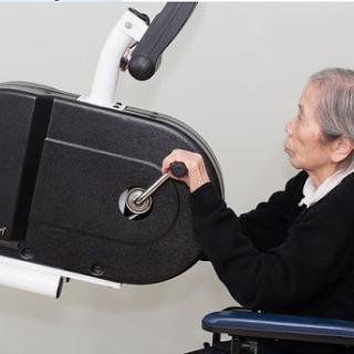 An elderly person using a rehabilitation exercise machine while seated in a wheelchair.