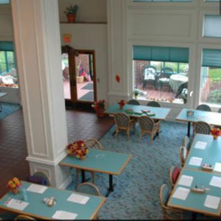 A bright and spacious dining area with multiple tables and chairs, featuring large windows and a view of the outside.