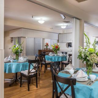 A well-decorated dining area with tables set for a meal, featuring floral arrangements and blue tablecloths.