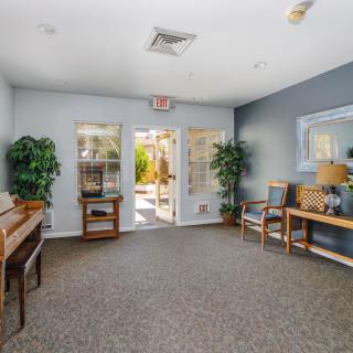 A well-lit room featuring a piano, seating area, and decorative plants.