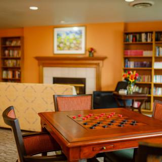 A cozy living room with a game of checkers set up on the table, surrounded by bookshelves and a fireplace.