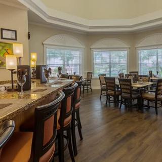 A cozy dining area with a bar and seating, featuring large windows and warm lighting.