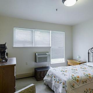 A simple, well-lit bedroom with a bed, dresser, and window.