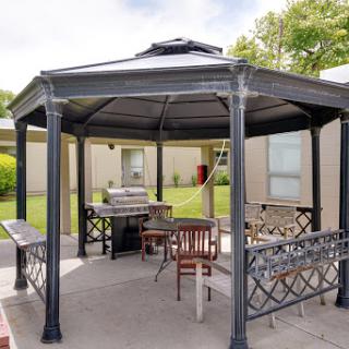 A stylish gazebo in a landscaped outdoor area, featuring seating and a grill.