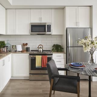 A modern kitchen with sleek white cabinets, stainless steel appliances, and a small dining area.
