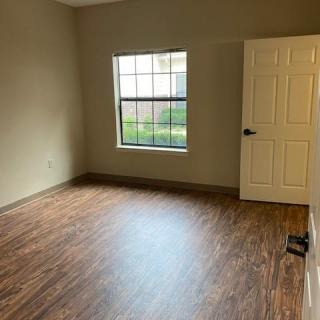 An empty room with wood flooring, a window, and a door.