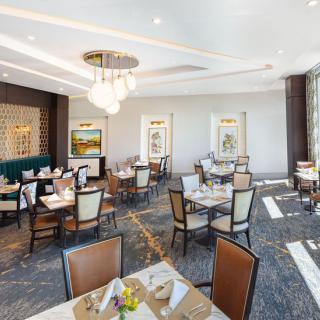 Elegant restaurant dining area with neatly arranged tables and chairs, featuring modern chandeliers and artwork on the walls.