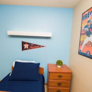 A small bedroom with blue walls, featuring a sports pennant and poster, a bed with blue bedding, and a wooden nightstand.