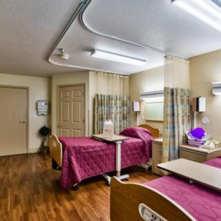 A healthcare facility room with two beds, separated by curtains.
