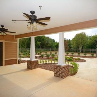 A spacious porch with ceiling fans overlooks a landscaped garden and driveway.