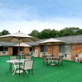 An outdoor seating area with tables, chairs, and umbrellas on a green artificial grass surface next to a brick building.