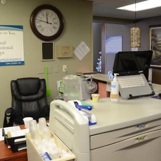 A view of an office reception area with a desk, clock, and seating.