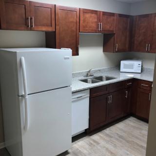 A compact kitchen with wooden cabinets, a refrigerator, microwave, and sink.