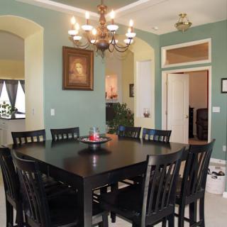 A cozy dining room with a dark wooden table and chairs, green walls, and an elegant chandelier.