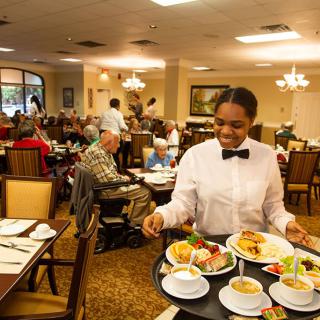 A waiter serves food to customers in a busy restaurant dining room.