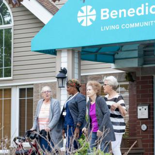 A group of seniors with a caregiver outside a nursing home called Benedict Living Community.