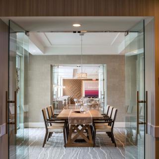 A modern dining room with a wooden table and chairs, enclosed by glass doors.