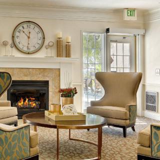A cozy living room with elegant seating around a fireplace, featuring stylish armchairs and a decorative wall clock.