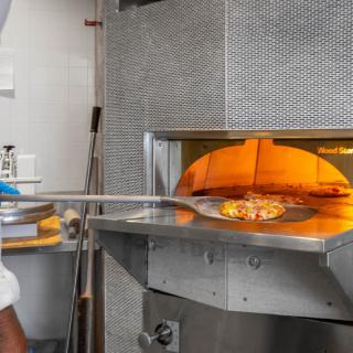 A pizza being placed into a wood-fired oven in a restaurant kitchen.