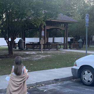 A child wrapped in a blanket enjoys the serene atmosphere of a park with a gazebo.