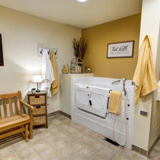 A cozy bathroom featuring a walk-in tub, a wooden bench, and decor with a warm color palette.