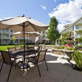 A sunny outdoor patio area with tables, chairs, and umbrellas in a well-landscaped garden setting.