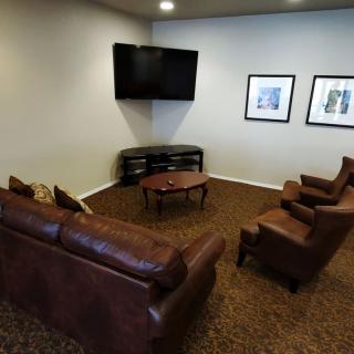 A cozy living room with leather couches, armchairs, a wall-mounted TV, and framed artworks on the wall.