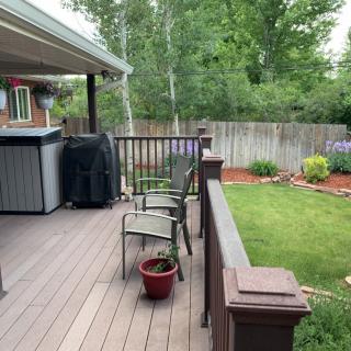 A peaceful backyard deck with chairs, a grill, and a view of the garden and lawn.
