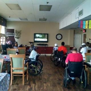 A community room in a nursing home with several people in wheelchairs watching television.