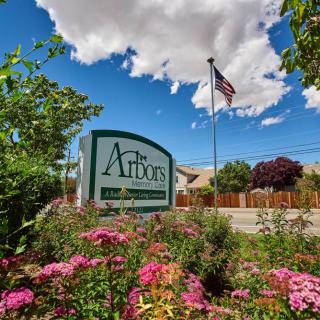 A vibrant outdoor scene with a sign surrounded by flowers, under a blue sky and clouds, featuring an American flag.