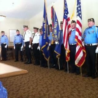 An honor guard stands in formation indoors, holding flags, including the American flag.