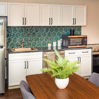 A modern kitchen featuring a green hexagonal backsplash, white cabinets, and a cozy dining area.