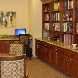 A cozy office space featuring a wooden bookshelf filled with books, a computer setup, and comfortable chairs.