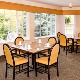 A cozy dining room with neatly arranged tables and chairs, illuminated by natural light coming through large windows.