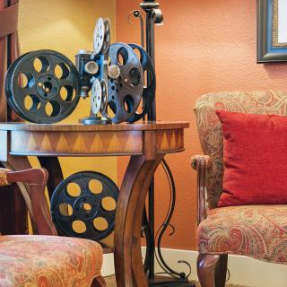 A cozy seating area featuring a vintage film projector on a wooden table, with plush armchairs and warm lighting.
