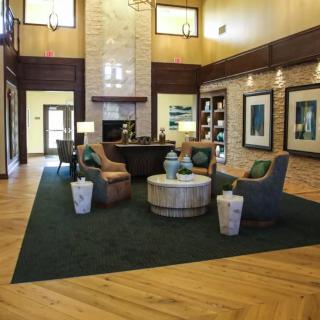 A cozy lobby with modern furniture and a wooden floor, featuring armchairs and a central table.