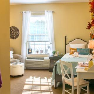 A cozy bedroom with a well-decorated interior featuring a comfortable chair, table, and bed by a window.