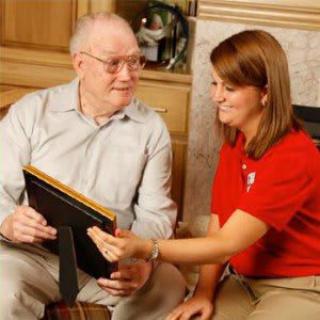 A caregiver assists an elderly person with a framed photo.