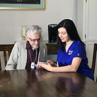 A caregiver assists an elderly man with a mobile device at home.