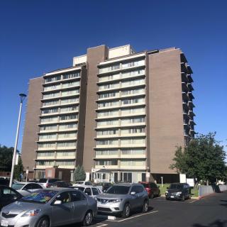 A high-rise apartment building with a parking lot in front, on a sunny day.