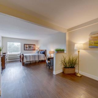 A modern open-concept living area with a cozy bedroom space, featuring wooden flooring, stylish furniture, and warm lighting.