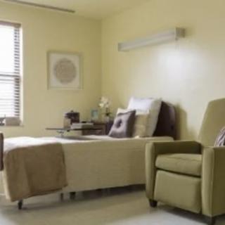 A well-lit hospital room with a bed and a comfortable chair next to a window.