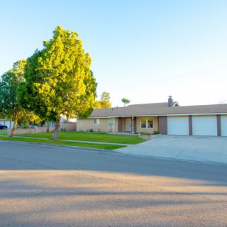 A suburban house with a large driveway and lush green lawn basking in the sunlight.