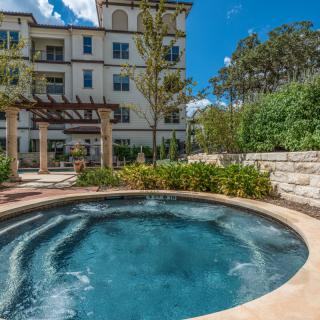 An outdoor hot tub with surrounding greenery in front of an apartment building on a sunny day.