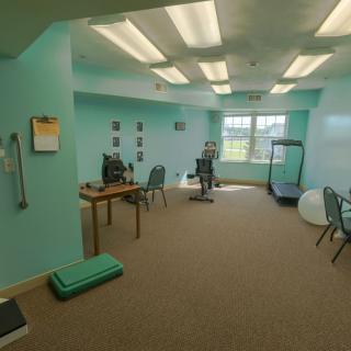 A spacious office with turquoise walls featuring desks, chairs, a computer, and exercise equipment including a treadmill.