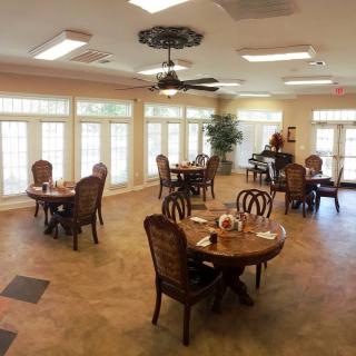A well-lit dining room with several tables and chairs, featuring large windows and a ceiling fan.