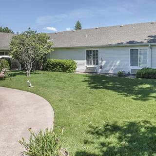 A peaceful backyard featuring a lush lawn, trees, and a patio area next to a house.