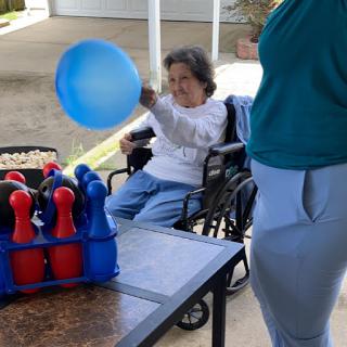 An elderly individual in a wheelchair participates in an outdoor bowling game, enjoying a sunny day.
